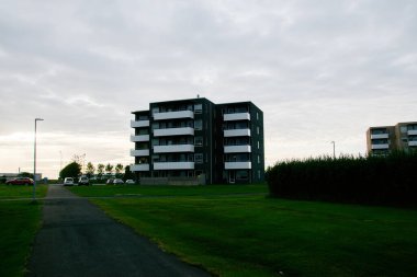 Arka planı çimen ve bulutlu gökyüzüne karşı balkonları olan küçük bir apartman..
