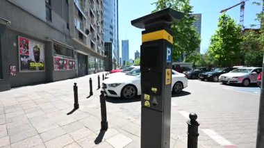 Varşova, Polonya - 2 Temmuz 2025: İnsanlar Polonya 'nın Varşova şehir merkezindeki hareketli bir caddede modern bir parkmetrenin yanından geçtiler.