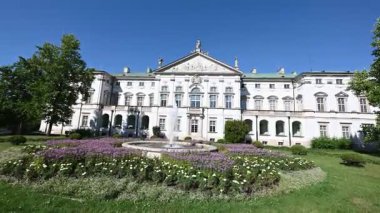 Güneşli bir günde faal bir çeşme ve canlı çiçek bahçeleriyle çarpıcı tarihi Cumhuriyet Sarayı cephesi.