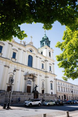 Varşova, Polonya - 02 Temmuz 2025 Polonya 'nın Varşova şehrinde yemyeşil ve park halindeki arabaları olan güzel tarihi bir Kutsal Haç kilisesi..