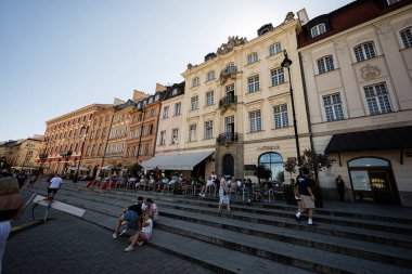 Varşova, Polonya - 2 Temmuz 2025: Büyüleyici binalar ve Polonya 'nın Varşova kentinde güneşli bir günün tadını çıkaran insanlar