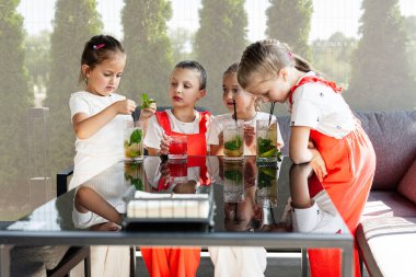 Çocuklar güneşli bir günde bir masanın etrafında oturmuş, ferahlatıcı içkilerin tadını çıkarıyorlar.