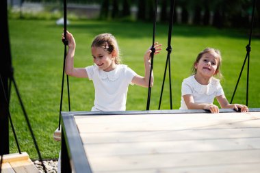 Salıncakta sallanan iki çocuk güneşli bir parkta eğleniyor.