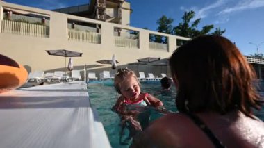 Anne ve bebek birlikte neşeli bir an paylaşıyor, sıcak açık havuzda oynuyorlar..