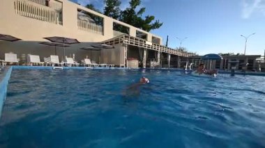 Çocuklar ve yetişkinler güneşli bir günde açık mavi bir havuzda ferahlatıcı bir yüzüşten hoşlanırlar..