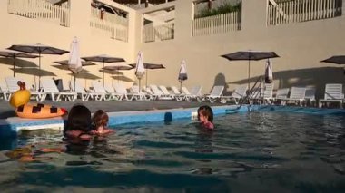 Çocuklar güzel bir yüzme havuzunda birlikte eğleniyor ve su sıçratıyorlar..