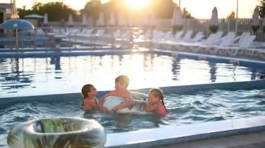 Neşeli çocuklar tatillerinin tadını çıkarıyorlar, büyük bir yüzme havuzunda oynuyorlar.