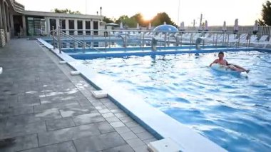 Çocuklar su sıçratır ve büyük bir yüzme havuzunda oynar. Eğlenceli bir yaz akşamının tadını çıkarırlar..