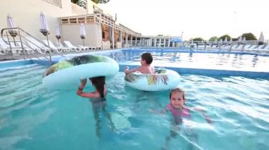 Neşeli çocuklar yaz tatilinin tadını çıkarıyor, su sıçratıyor ve havuzda yüzücülerle eğleniyor..