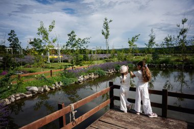 Beyaz elbiseli iki çocuk manzaralı bir göletin yakınındaki ahşap bir güverteyi keşfediyorlar.