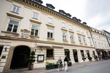 Krakow, Polonya - 08 Temmuz 2025: Krakow caddesinde yürüyen insanlarla dolu tarihi bir binanın ön cephesi.