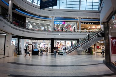 Krakow, Polonya - 08 Temmuz 2025: Çeşitli perakende mağazaları ve yürüyen merdivenleri olan çok katlı bir alışveriş merkezini keşfeden insanlar