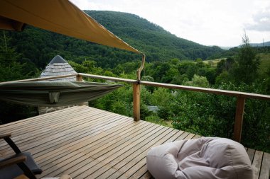 Tahta güverte, hamak, fasulye torbası ve orman manzarası..