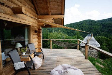 Huzurlu orman ve dağ manzarası sunan taşralı kabin güvertesi, rahat dış mobilyalarla.