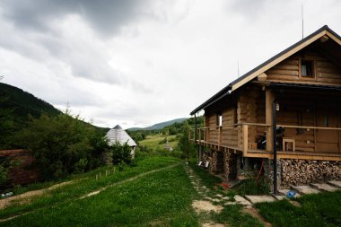 Etrafı yeşillik ve doğa ile çevrili ahşap kulübe bulutlu bir gökyüzü altında..