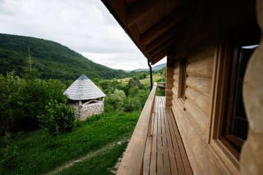 Kırsal manzaralı, ağaçlar ve yemyeşil tepelerle çevrili taşralı ahşap kulübe.