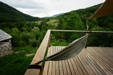 Ahşap bir platformda, yemyeşil bir orman ve tepelerin manzarasını sunan bir hamak..
