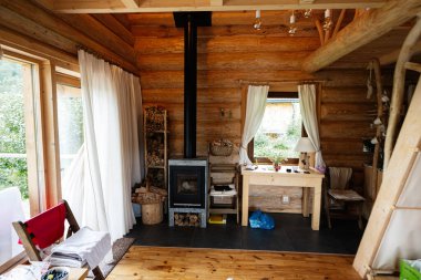 Sıcak ve davetkar bir kulübe köşesinde odun sobası ve doğal ahşap mobilyalar var.