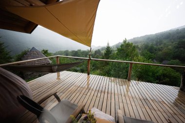 Bulutlu gökyüzünün altında yağmurlu dağ manzaralı sakin ahşap bir teras.