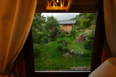 Yeşil ormandaki sakin ahşap kulübe, pencereden güzel görünüyor..