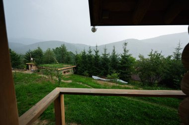 Yeşillik, dağlar ve bulutlu gökyüzünün altında bir balkon barındıran manzaralı bir yer..