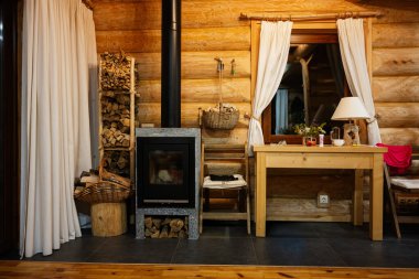 Odanın içinde şömine, ahşap yığını, kütük duvarlar ve rahat bir dekor var..