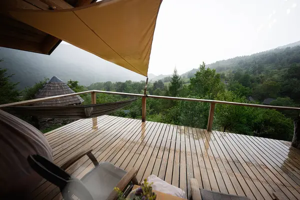Bulutlu gökyüzünün altında yağmurlu dağ manzaralı sakin ahşap bir teras.