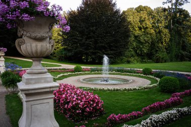 Yaz boyunca zarif bir bahçede canlı çiçeklerle çevrili bir çeşme, Lancut, Polonya.