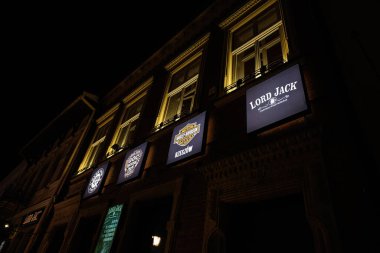 Rzeszow, Polonya - 22 Ağustos 2025: Canlı iş işaretleri gösteren ışıklı bir Lord Jack binasının olduğu gece sokak manzarası.