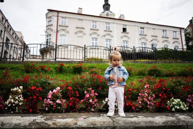 Çiçeklerle dolu tarihi bir binanın önünde sıradan giyinmiş küçük bir çocuk.