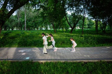 Çocuklar yemyeşil bir parkta kaldırım tebeşiri ile çizilmiş seksek oynamaktan mutlu olurlar.