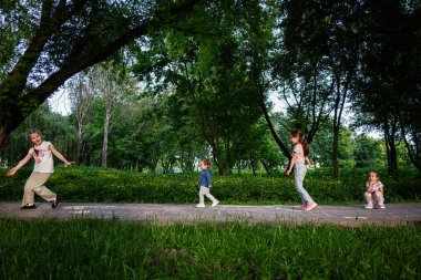 Dört çocuk güneş ışığı ve ağaçların altındaki canlı bir parkta aktif olarak birlikte oynuyorlar..