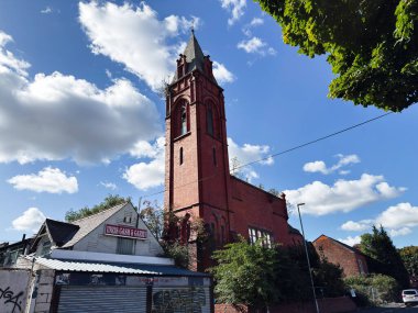 Manchester, İngiltere - 23 Eylül 2025: Manchester, İngiltere 'de açık mavi gökyüzünün altında terk edilmiş bir mağaza vitrininin yanında terk edilmiş uzun tuğla kilise kulesi.