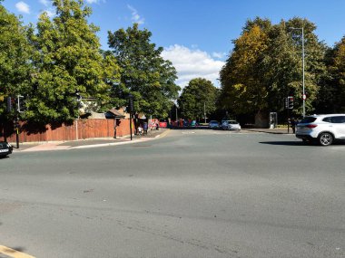 Manchester, İngiltere - 23 Eylül 2025: Park halindeki arabaların, yayaların, yeşilliklerin ve kentsel arkaplanın yer aldığı güneşli Manchester kavşağı.