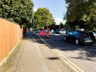 Manchester, İngiltere - 23 Eylül 2025: Güneşli bir günde kaldırım boyunca yol işaretleri, bariyerler ve arabalarla dolu Manchester Caddesi.