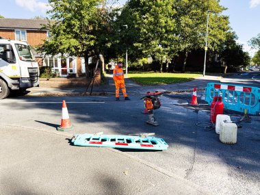 Manchester, İngiltere - 23 Eylül 2025: Manchester 'daki inşaat sahnesinde turuncu güvenlik donanımı, engeller ve yol ekipmanı kullanan bir işçi.