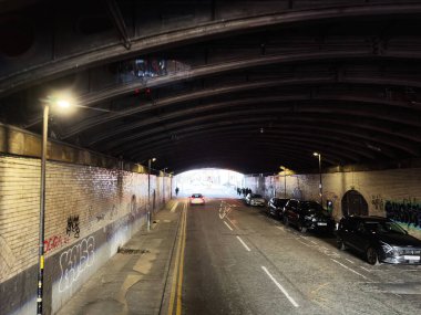 Manchester, İngiltere - 23 Eylül 2025: Graffiti, Manchester 'da park etmiş arabalar ve yol boyunca sokak lambaları olan loş bir alt geçidi kapladı.