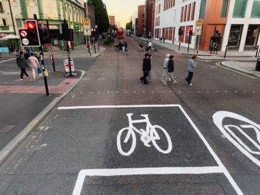 Manchester, İngiltere - 23 Eylül 2025: Manchester 'da yaya geçidinde bisiklet yolu ve gün batımının yanında yayaları gösteren şehir sokak sahnesi.