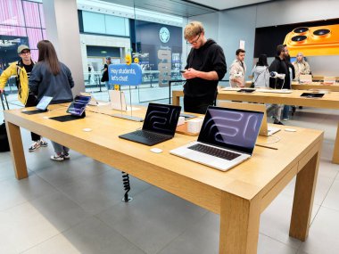 Manchester, İngiltere - 26 Eylül 2025: Müşteriler ve öğrenciler parlak bir Apple mağazasının içindeki masalarda dizüstü bilgisayarlara bakıyorlar.