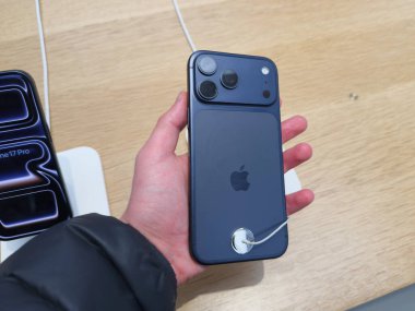 Manchester, İngiltere - 29 Eylül 2025: Mavi iPhone 17 Pro 'nun elinde üçlü kameralar, ahşap bir vitrin masasına bağlı güvenlik kablosu.