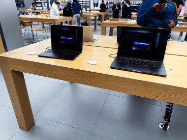 Manchester, İngiltere - 29 Eylül 2025: MacBook Pro, işlek bir teknoloji perakende mağazasında, müşterilerin keşif cihazlarıyla birlikte ahşap bir masada dizüstü bilgisayar..