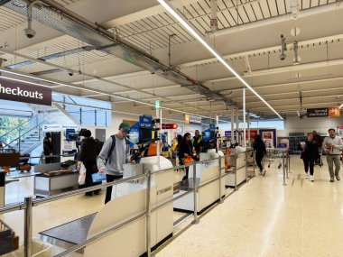 Salford, İngiltere - 25 Eylül 2025: Müşteriler, modern, parlak bir Sainsbury mağazasında çalışan personele yardım ederken, kendilerini kontrol ediyorlar.