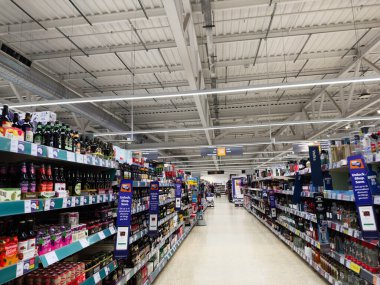 Salford, İngiltere - 25 Eylül 2025: Geniş bir Sainsbury süpermarket koridoru içecek şişeleri, parlak tabelalar ve temiz raflarla dolu.