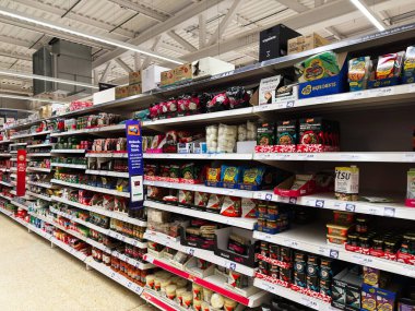 Salford, İngiltere - 25 Eylül 2025: Sainsbury, İngiltere 'de organize edilmiş konserve, makarna ve kuru ürünlerle dolu parlak süpermarket koridoru.