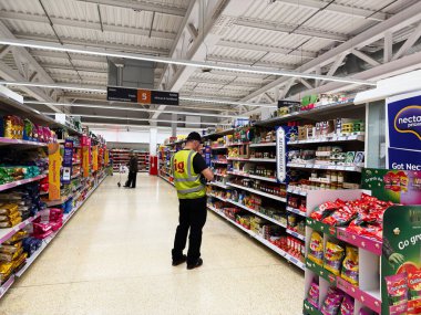 Salford, İngiltere - 25 Eylül 2025: Sainsbury 'nin bir süpermarket çalışanı parlak, iyi ışıklandırılmış koridorlarda ürünler araştırıyor.