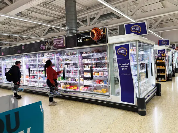 Salford, İngiltere - 25 Eylül 2025: Müşteriler serin bir süpermarkette koridorlara göz gezdirdiler, tatlı ve bakkaliye seçtiler.