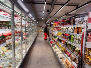 Manchester, İngiltere - 25 Eylül 2025: İyi aydınlatılmış Seul Plaza süpermarket şeridinde bir müşteri soğutulmuş ve atıştırmalık raflardan eşyalar seçiyor.