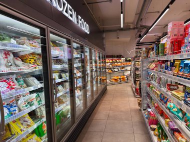 Manchester, İngiltere - 25 Eylül 2025: Solunda cam soğutmalı üniteler ve sağında raflar dolusu atıştırmalıklar bulunan Bright Seul Plaza market koridoru.