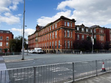 Manchester, İngiltere - 25 Eylül 2025: Manchester şehir caddesi boyunca minibüsleri, yayaları ve metal parmaklıkları olan kırmızı tuğlalı şehir binası.