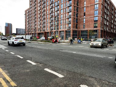 Manchester, İngiltere - 25 Eylül 2025: Manchester City caddesinde işçilerin ve trafiğin bulunduğu kırmızı tuğlalı bir apartmanın yanında yoğun kentsel inşaat sahnesi.
